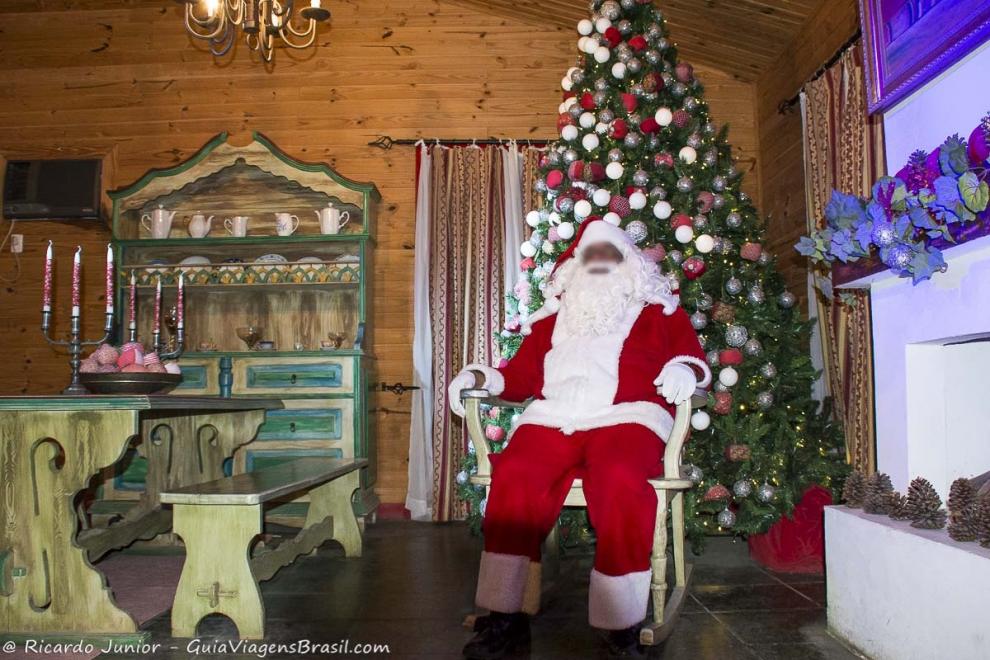 Imagem do Papai Noel sentado em frente a árvore de Natal recebendo turistas em Penedo.